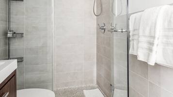 A modern bathroom with a glass shower enclosure, a toilet, and a vanity with a towel rack.