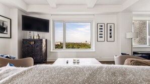Un salón moderno con un amplio ventanal, un televisor de pantalla plana y vistas a un paisaje urbano.