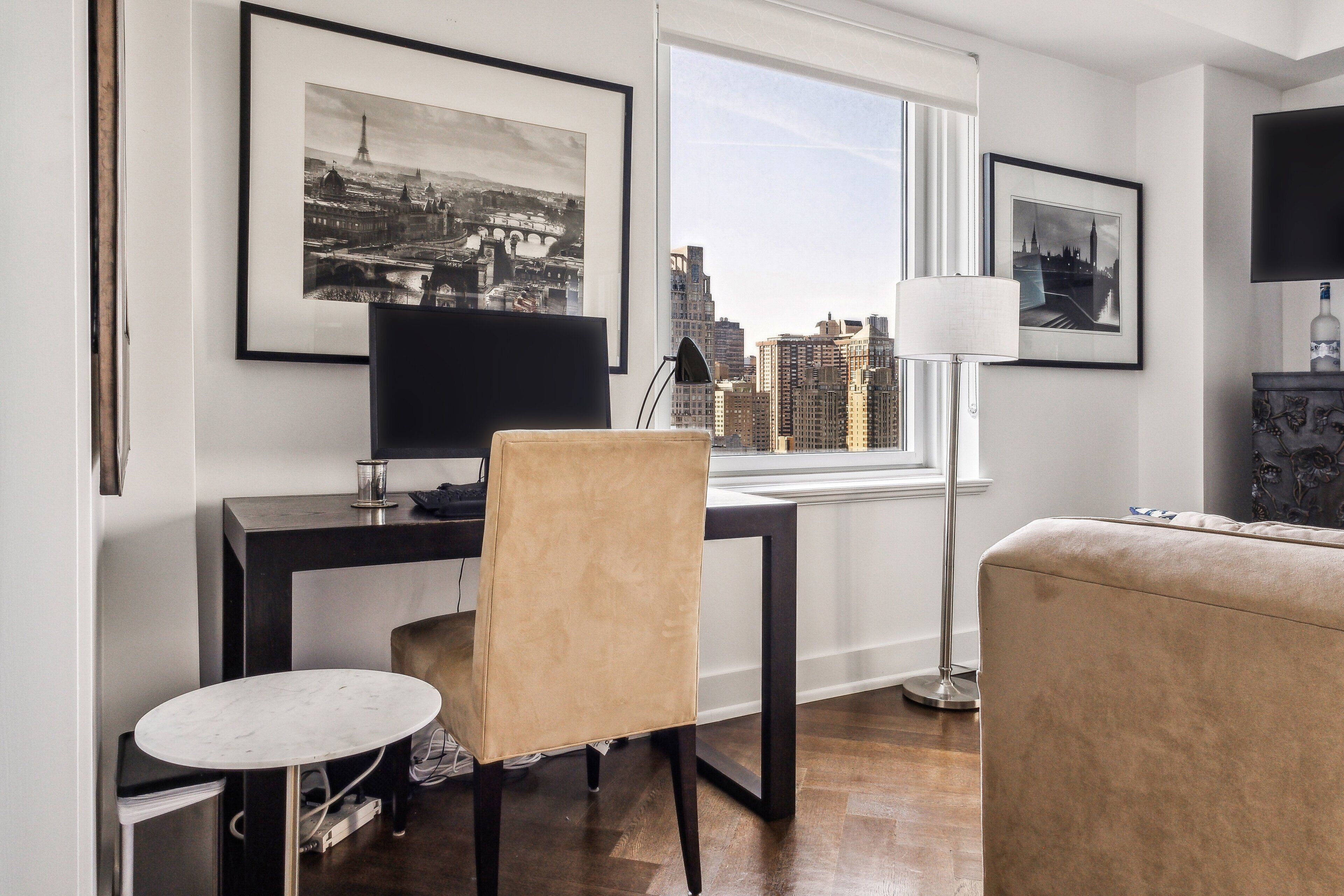 A modern living room with a desk, chair, and a view of a cityscape through a large window.