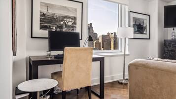 A modern living room with a desk, chair, and a view of a cityscape through a large window.