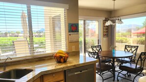 A kitchen with a built-in dishwasher, a fruit bowl on the counter, and a dining area with a table and chairs.