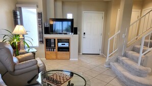 A spacious living room with a glass coffee table, a comfortable sofa, a television, and a staircase.