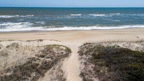 Ein Strand mit einem sandigen Pfad, der zum Wasser führt, umgeben von Dünen.