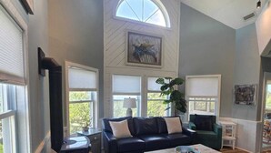Ein geräumiges Wohnzimmer mit hoher Decke, großen Fenstern, einem Deckenventilator und einem Kamin.