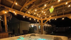 A hot tub with bubbling water, surrounded by wooden beams and string lights. - Seabreeze garden oasis, jacuzzi, golf, mins ->beaches (Largo)