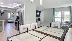 A modern kitchen with a dining area, stainless steel appliances, and a large window providing natural light. - Seabreeze garden oasis, jacuzzi, golf, mins ->beaches (Largo)