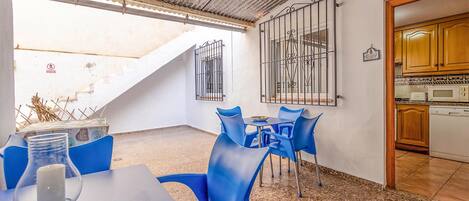 A small dining area with blue chairs and a table, a kitchen with wooden cabinets, and a staircase leading to an upper level.