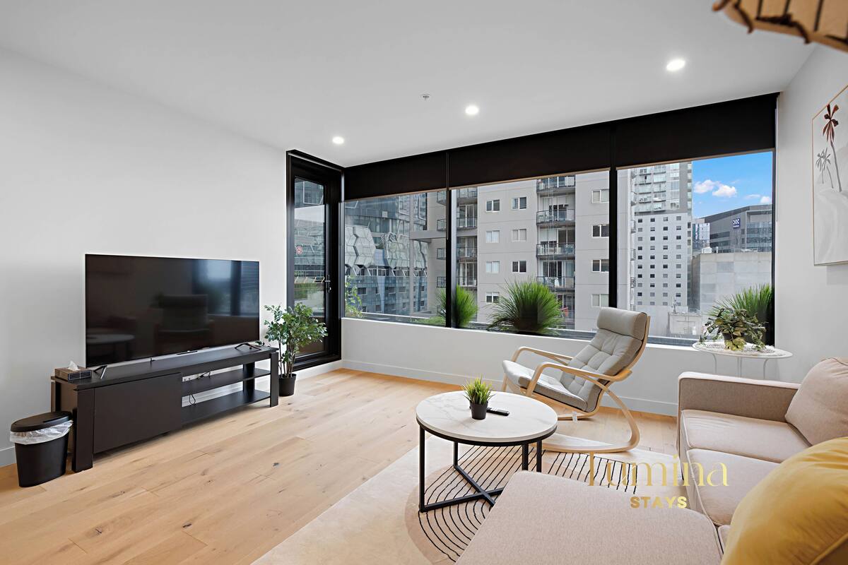 Een moderne woonkamer met een televisie, bank, stoelen en een groot raam met uitzicht op de stad.