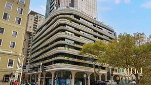 A modern high-rise hotel with a unique curved facade, multiple balconies, and a prominent entrance with a sign. - Lumina Stays - Aspire (Melbourne)