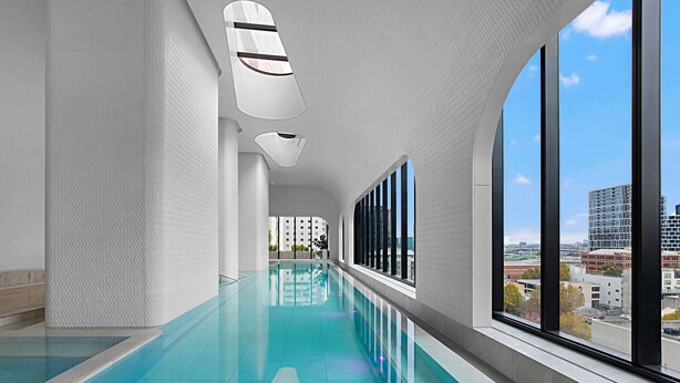 A modern indoor swimming pool with a clear view of the cityscape through large windows. - Lumina Stays - Aspire (Melbourne)