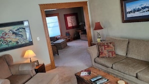 A living room with a sofa, armchair, and coffee table. There is a painting on the wall and a lamp on the side table.