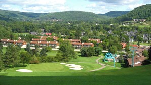A golf course with a large green, a blue swing set, and a row of red-roofed buildings. - Not Your Everyday Mini Chalet, foot of Holiday Valley Resort! Walk to Downtown (Ellicottville)