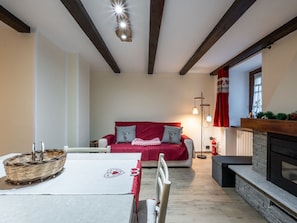 A cozy living room with a fireplace, a red sofa, and a dining area with a basket and table. - Maison Bonheur by Interhome (La Salle)