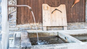 Ein rustikaler Steinbrunnen, in den Wasser in ein hölzernes Tröge fließt.