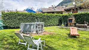 Eine Terrasse mit Tisch und Stühlen, umgeben von einer Hecke und Blick auf Berge.