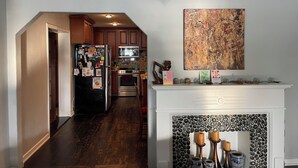 Una cocina con armarios de madera, un refrigerador negro, un microondas y una estufa. Hay una chimenea con piedras decorativas y velas.