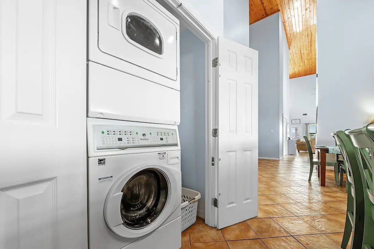 Un cuarto de lavado con lavadoras y secadoras apiladas, una cesta y techo de madera.