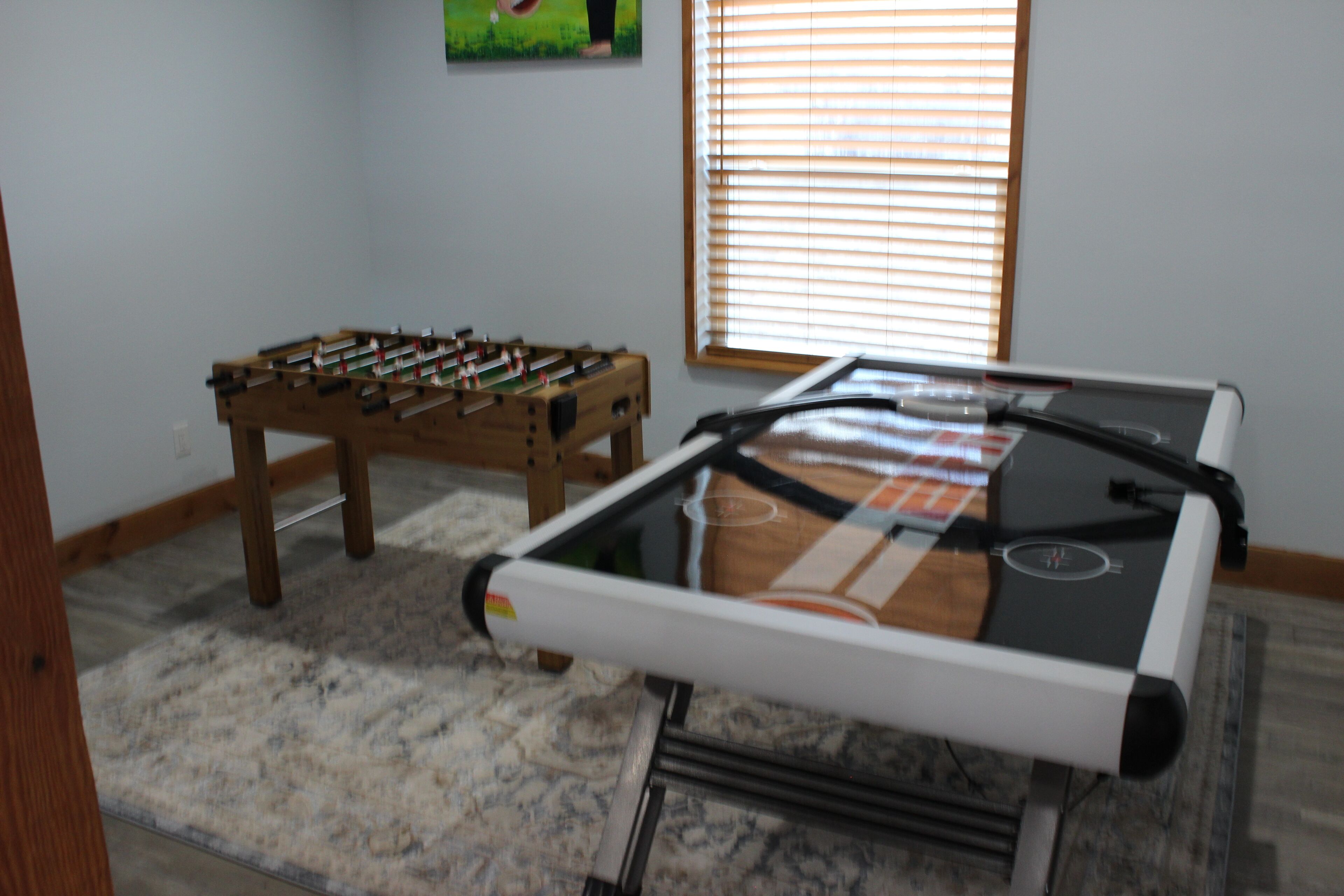 Una habitación con mesa de futbolín, mesa de billar y una ventana con persianas.