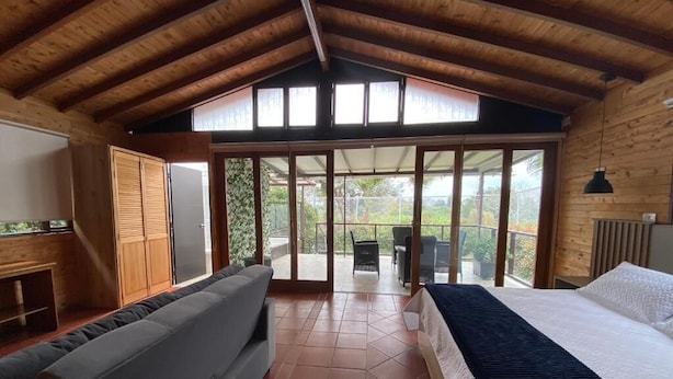 A room with a bed, a sofa, and a sliding glass door leading to an outdoor area with a view of greenery. - Finca Hotel 12 Palmas (Rionegro)