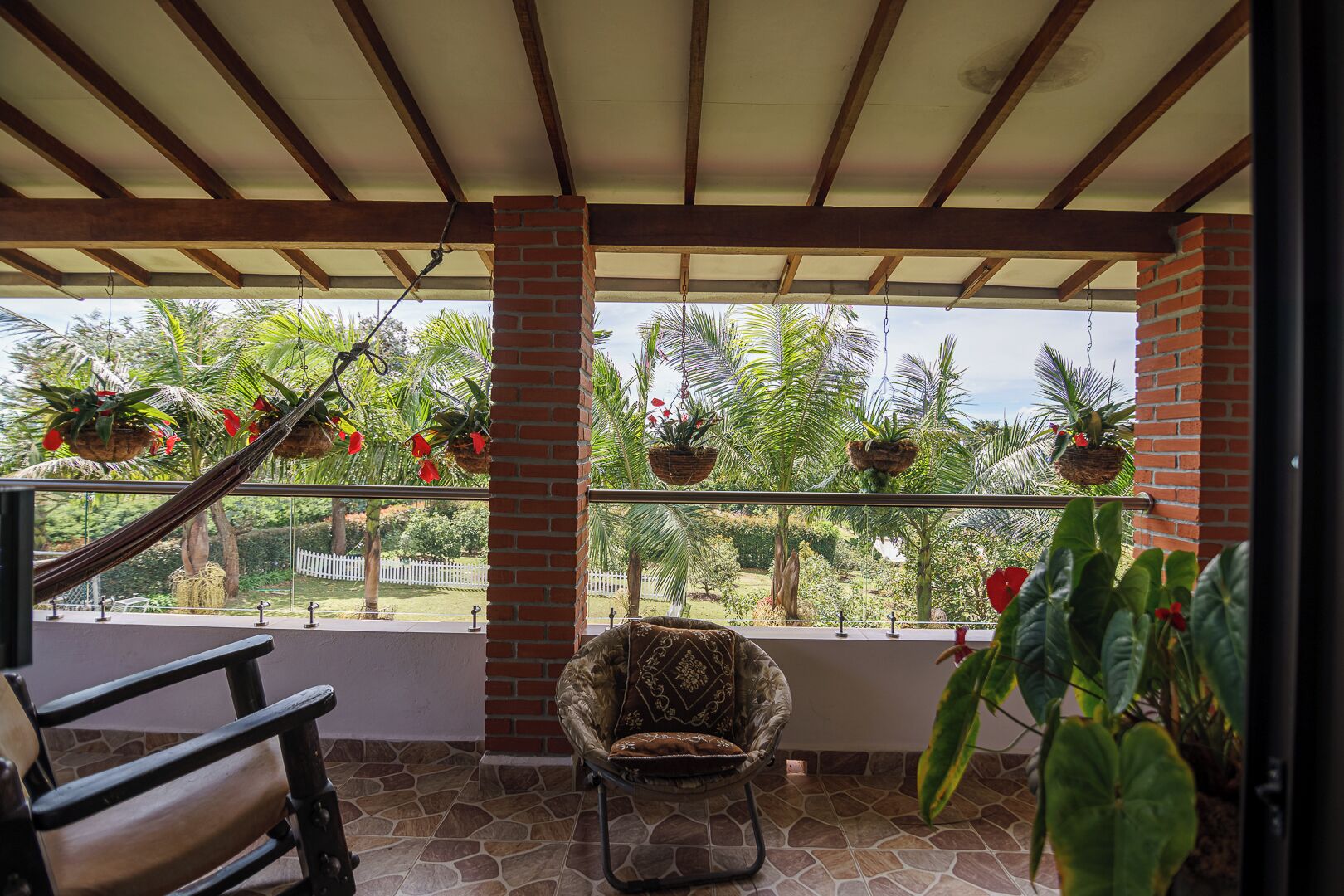 Un balcon abrité, doté d’une chaise, de jardinières suspendues et offrant une vue sur un jardin.