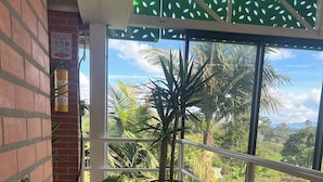 A balcony with potted plants, a brick wall, and a view of a lush landscape. - Finca Hotel 12 Palmas (Rionegro)