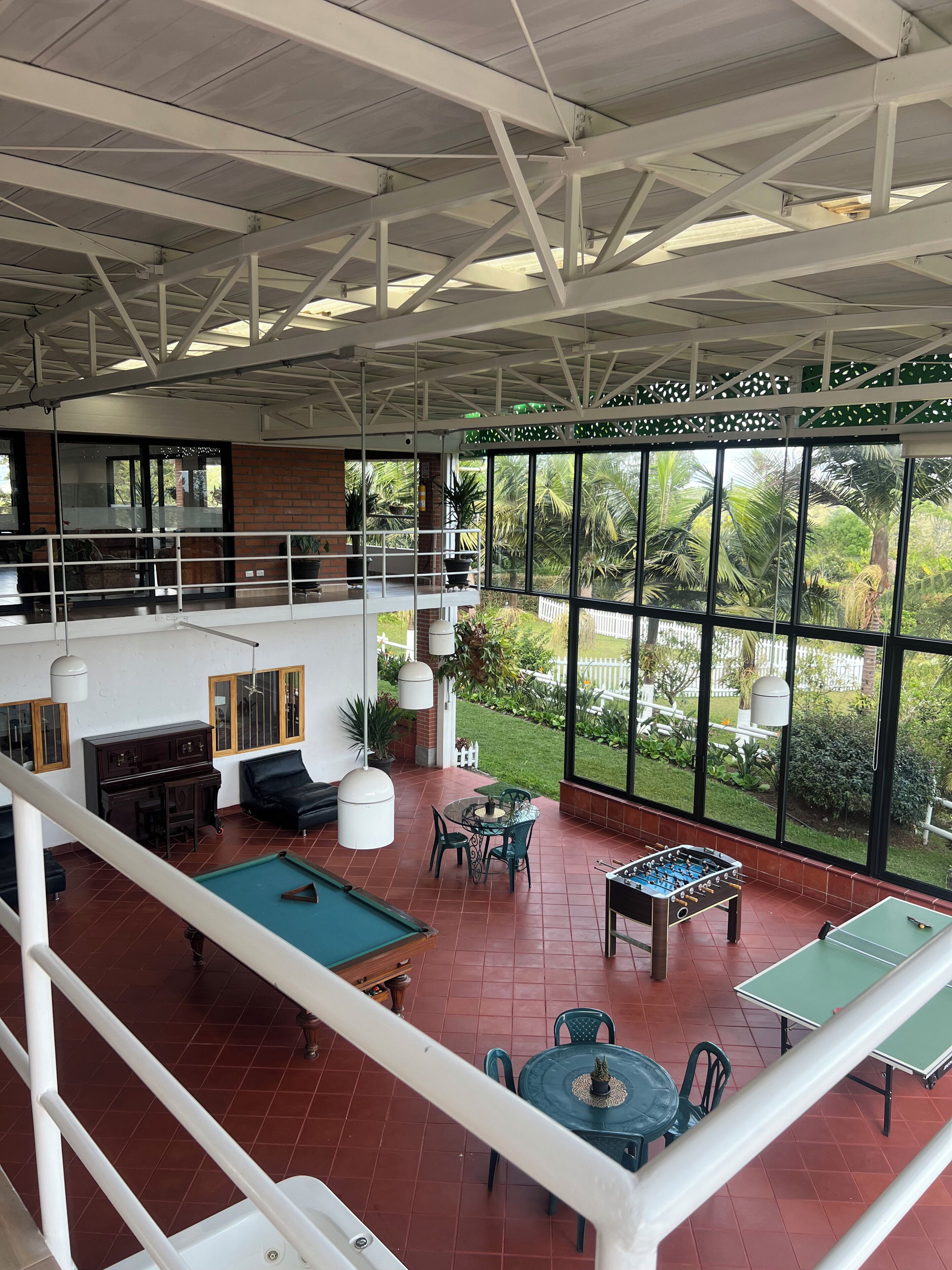 A spacious indoor area with a pool table, foosball table, and a ping pong table. There is a balcony with a view of a garden.