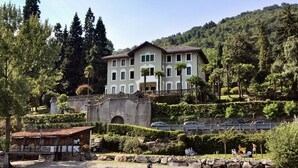 A large, multi-story building with a symmetrical facade, surrounded by lush greenery and a mountainous backdrop. - Villa Ceriana by Interhome (Ghiffa)
