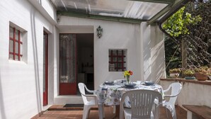 A patio with a table set for four, surrounded by white plastic chairs, under a covered area with a metal roof. - Il Castagneto by Interhome (Arma di Taggia)