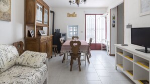 A cozy living room with a wooden cabinet, a dining table with chairs, a sofa with a musical note pattern, a television on a stand, and a 'Smile' sign on the wall. - Il Castagneto by Interhome (Arma di Taggia)