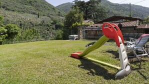 A grassy outdoor area with a playground, including a slide and swings, in a rural setting with hills in the background. - Il Castagneto by Interhome (Arma di Taggia)