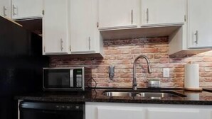 Cozinha com armários brancos, painel de backsplash de tijolo, pia de aço inoxidável e lava-louças preta.