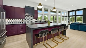 Een moderne keuken met een centraal eiland, barstoelen en uitzicht op het groen door grote ramen.