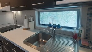 Una cocina moderna con armarios oscuros, un lavamanos de acero inoxidable, un microondas y un ventanal con un diseño de hojas.