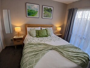 Une chambre d’hôtel avec un lit, deux lampes de chevet, une tête de lit et deux tableaux encadrés accrochés au mur.