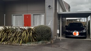 Un edificio moderno con una puerta roja, un área de estacionamiento techada y un coche negro estacionado en su interior.