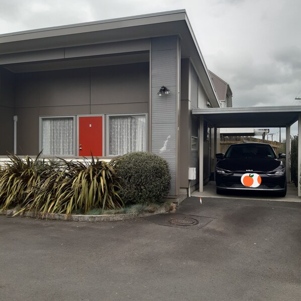 A modern building with a red door, a covered parking area, and a black car parked inside.