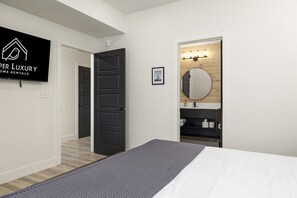 Un dormitorio con una cama, un tapete gris, una puerta negra, un espejo y una tocador con estantes de madera.