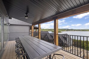 Una terraza al aire libre techada con una mesa larga y sillas, con vistas a un lago y colinas.