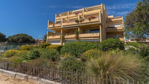 Un edificio de varios pisos con balcones, rodeado de abundante vegetación y una valla de madera.
