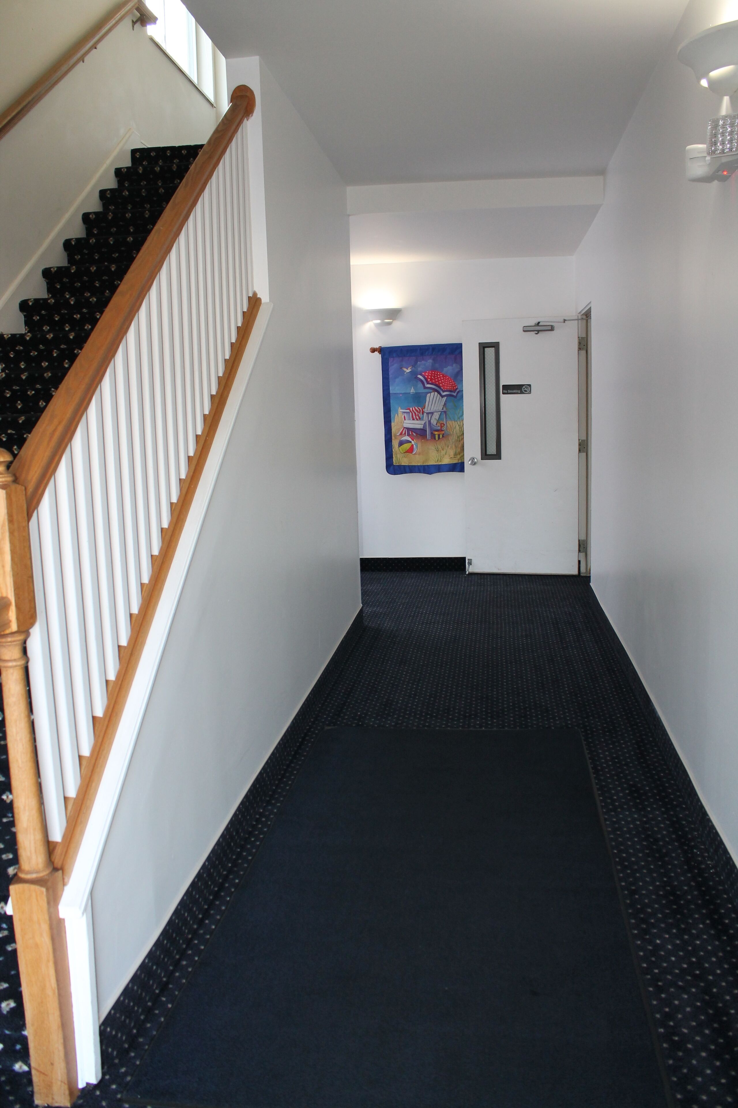 A hallway with a wooden staircase on the left, a black carpeted floor, and a door with a colorful poster on the wall.
