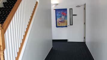 A hallway with a wooden staircase on the left, a black carpeted floor, and a door with a colorful poster on the wall.