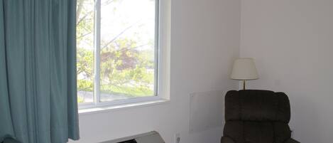 A room with a window, an air conditioning unit, a chair, and a lamp.