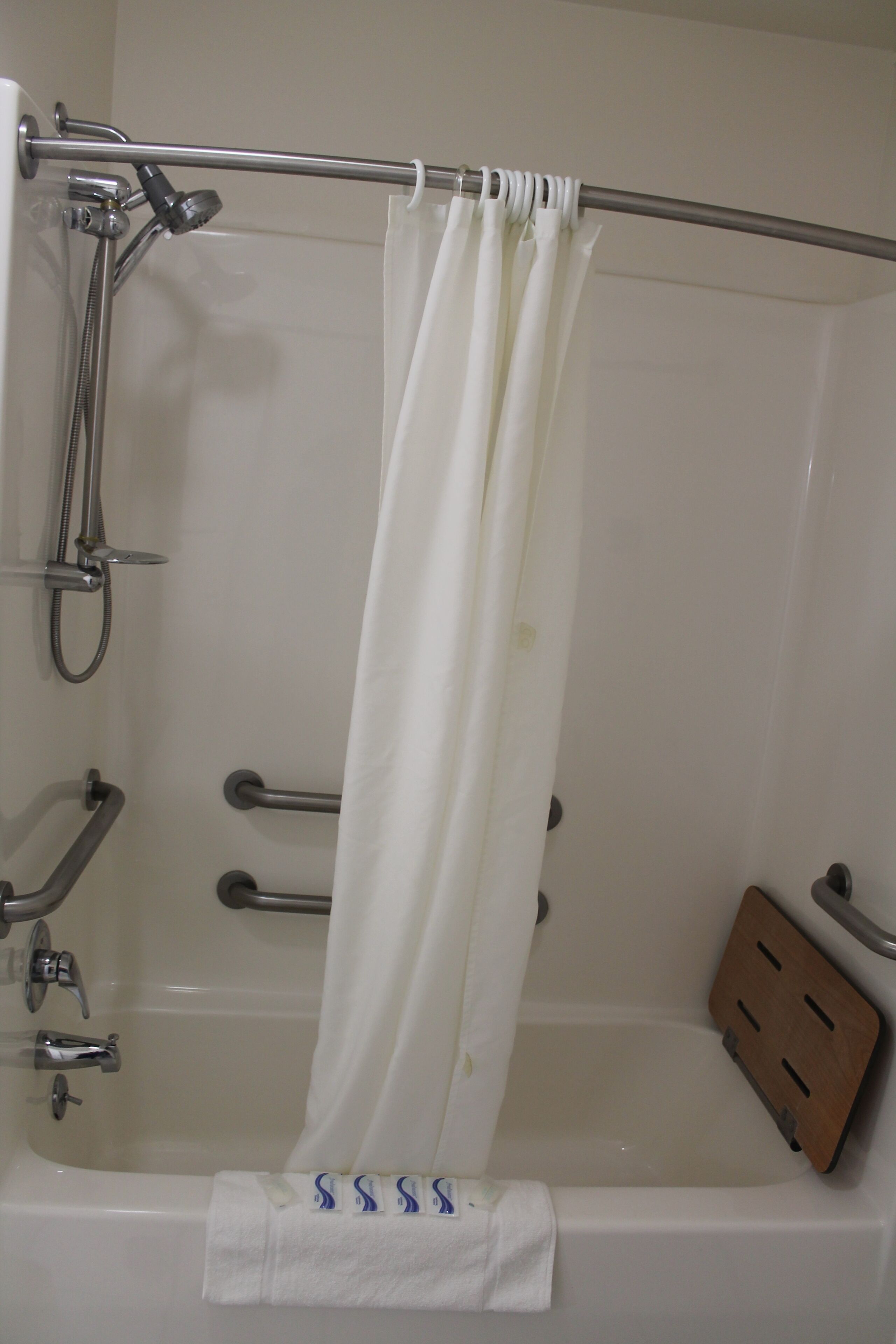 A bathroom with a bathtub, a showerhead, a towel rack, and a wooden bath mat.