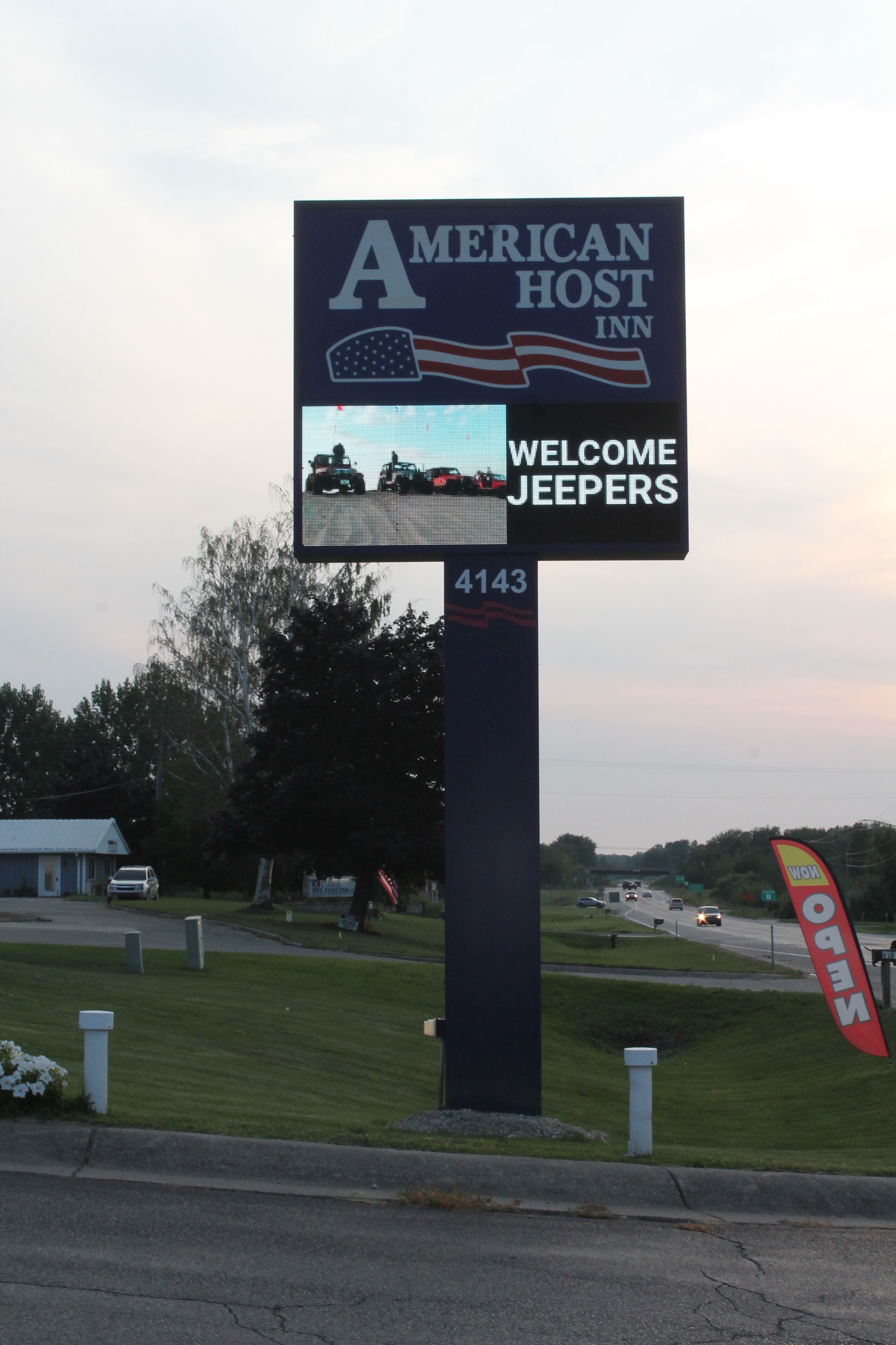 Letrero del American Host Inn con un mensaje de bienvenida para Jeepers, el número 4143 y una vista de una carretera con vehículos.