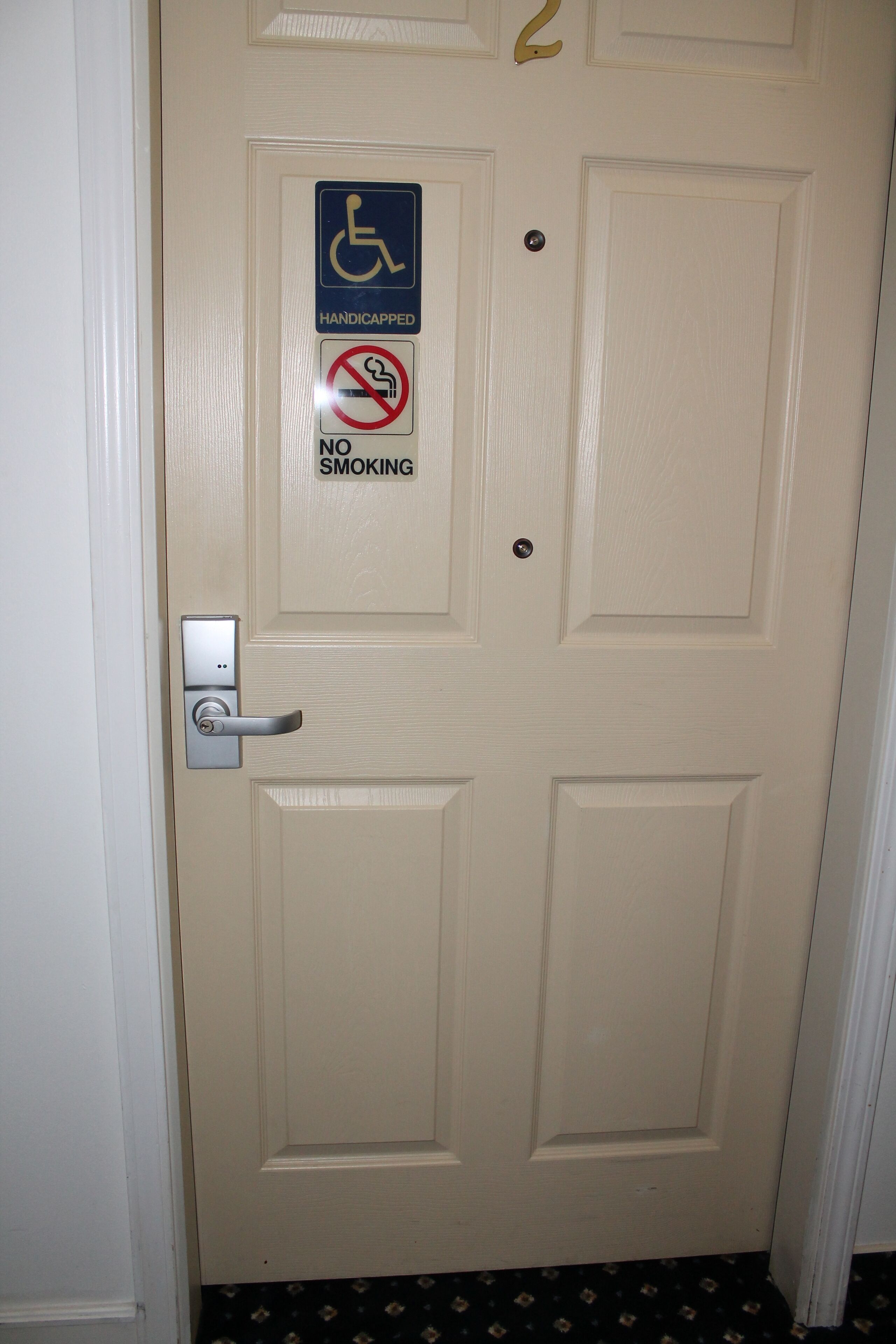 Une porte avec un panneau indiquant qu’elle est accessible aux personnes handicapées, un panneau interdisant de fumer et un interphone.