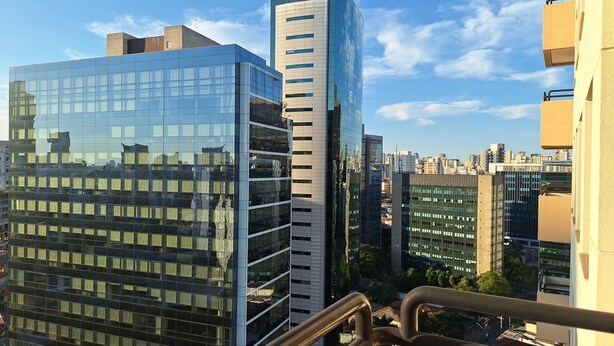 A high-rise building with reflective glass windows, surrounded by other modern buildings and a clear sky. - HOTEL FARIA LIMA (São Paulo)