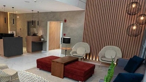 A modern hotel lobby with a reception desk, seating area with sofas and chairs, and a large potted plant. - HOTEL FARIA LIMA (São Paulo)