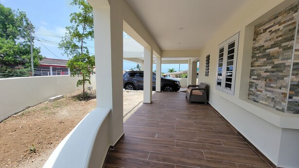 A covered outdoor area with a tiled floor, a stone wall, and a parked SUV.