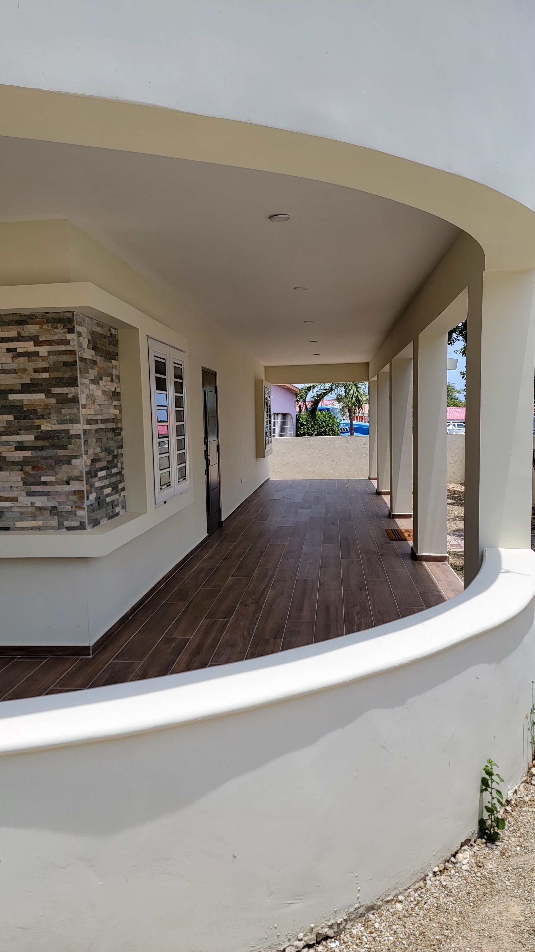 A covered corridor with a stone wall on one side and a white wall on the other, leading to a door.