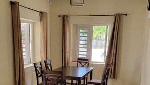A dining area with a table and chairs, a sofa, and windows with curtains.